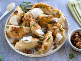Golden Polish pierogi arranged on a rustic wooden plate, topped with caramelized onions and fresh herbs, with melted butter glistening on top