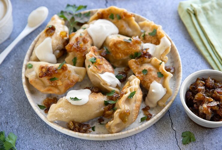 Golden Polish pierogi arranged on a rustic wooden plate, topped with caramelized onions and fresh herbs, with melted butter glistening on top