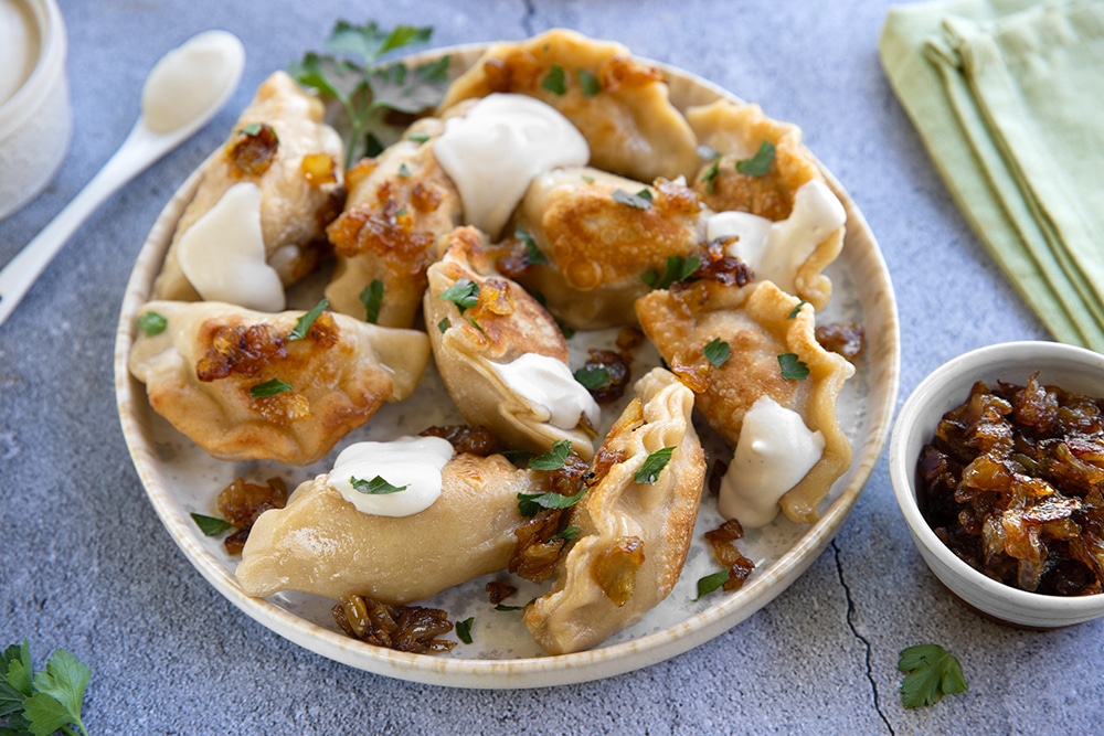 Golden Polish pierogi arranged on a rustic wooden plate, topped with caramelized onions and fresh herbs, with melted butter glistening on top