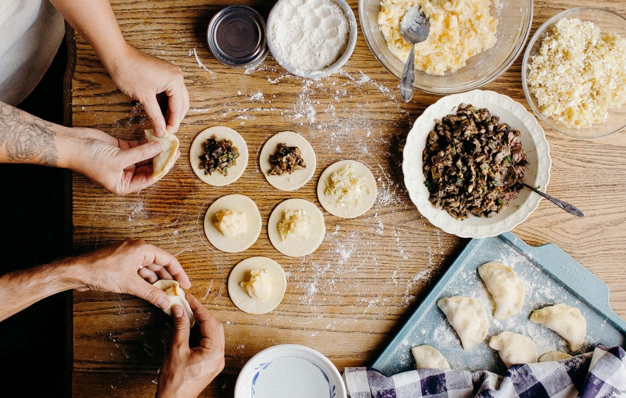 Hands folding pierogi dough around filling, showing the traditional crimping technique with flour-dusted work surface