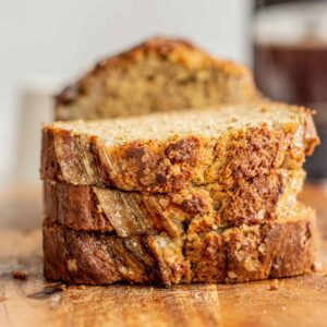 Sliced banana bread on a rustic wooden cutting board with golden brown crust and incredibly moist crumb visible