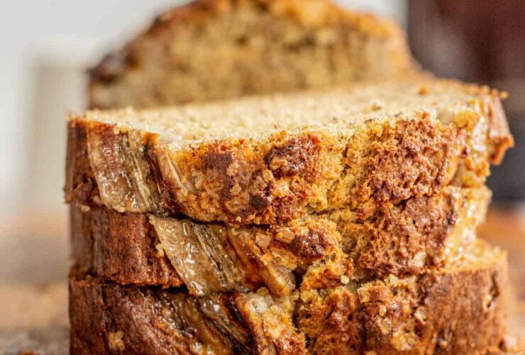 Sliced banana bread on a rustic wooden cutting board with golden brown crust and incredibly moist crumb visible