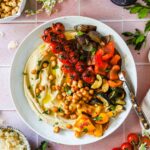 Roasted chickpea and vegetable hummus bowl beautifully plated with golden crispy chickpeas, creamy hummus, fresh cucumber, tomatoes, and herbs overhead shot
