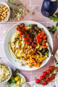 Roasted chickpea and vegetable hummus bowl beautifully plated with golden crispy chickpeas, creamy hummus, fresh cucumber, tomatoes, and herbs overhead shot
