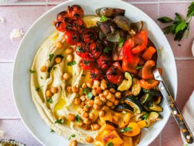 Roasted chickpea and vegetable hummus bowl beautifully plated with golden crispy chickpeas, creamy hummus, fresh cucumber, tomatoes, and herbs overhead shot