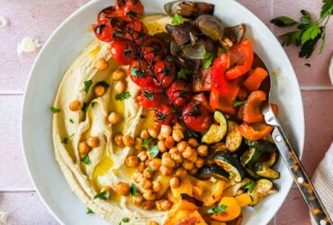 Roasted chickpea and vegetable hummus bowl beautifully plated with golden crispy chickpeas, creamy hummus, fresh cucumber, tomatoes, and herbs overhead shot