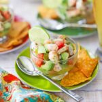 Gorgeous bowl of shrimp ceviche with vibrant pink shrimp, diced vegetables, and fresh herbs, garnished with lime wedges and served with crispy tortilla chips