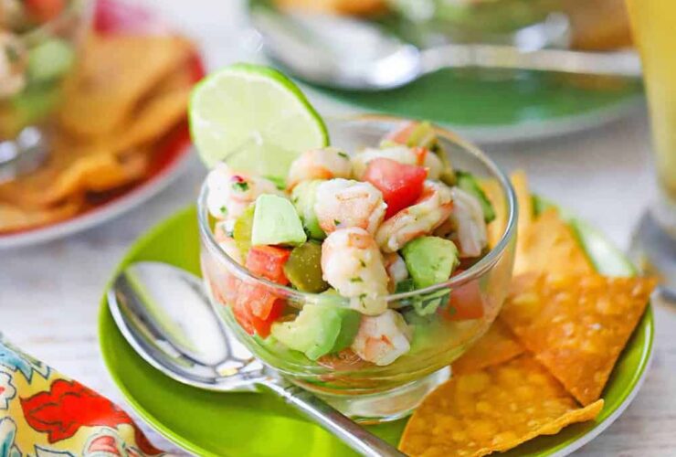Gorgeous bowl of shrimp ceviche with vibrant pink shrimp, diced vegetables, and fresh herbs, garnished with lime wedges and served with crispy tortilla chips