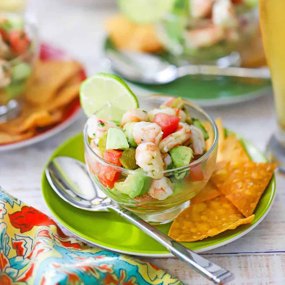 Gorgeous bowl of shrimp ceviche with vibrant pink shrimp, diced vegetables, and fresh herbs, garnished with lime wedges and served with crispy tortilla chips