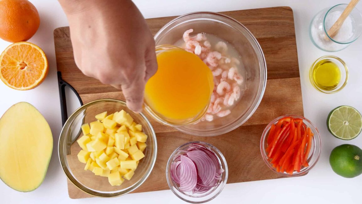 Step-by-step preparation shot showing diced shrimp marinating in lime juice with colorful vegetables being added