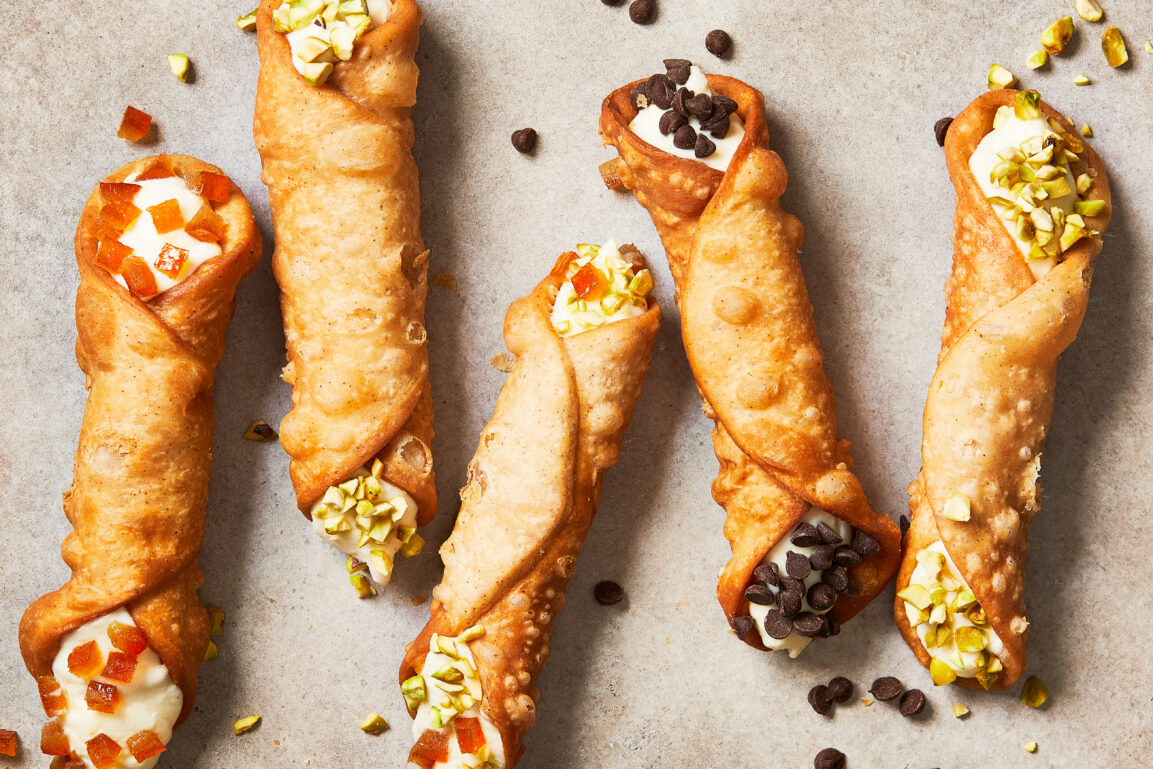 Close-up cross-section of a cannoli showing the contrast between the golden crispy shell and creamy white filling, with visible chocolate chips and pistachios