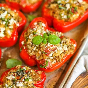 Overhead shot of colorful stuffed bell pepper boats filled with ground turkey and quinoa, garnished with fresh herbs and crumbled feta on a rustic wooden table