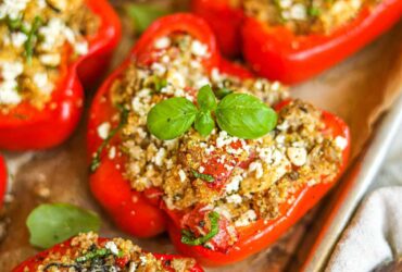 Overhead shot of colorful stuffed bell pepper boats filled with ground turkey and quinoa, garnished with fresh herbs and crumbled feta on a rustic wooden table