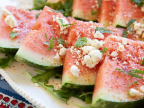 Elegant watermelon feta mint salad beautifully arranged on a white ceramic platter with chunks of pink watermelon, creamy white feta crumbles, and bright green mint leaves, garnished with lime wedges