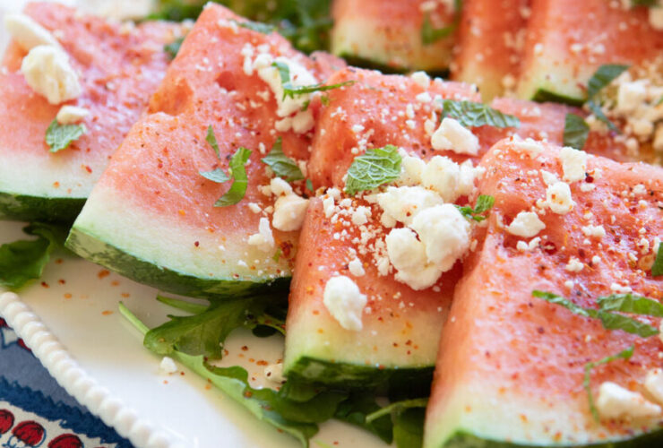 Elegant watermelon feta mint salad beautifully arranged on a white ceramic platter with chunks of pink watermelon, creamy white feta crumbles, and bright green mint leaves, garnished with lime wedges