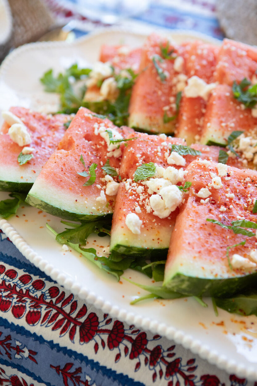 Elegant watermelon feta mint salad beautifully arranged on a white ceramic platter with chunks of pink watermelon, creamy white feta crumbles, and bright green mint leaves, garnished with lime wedges