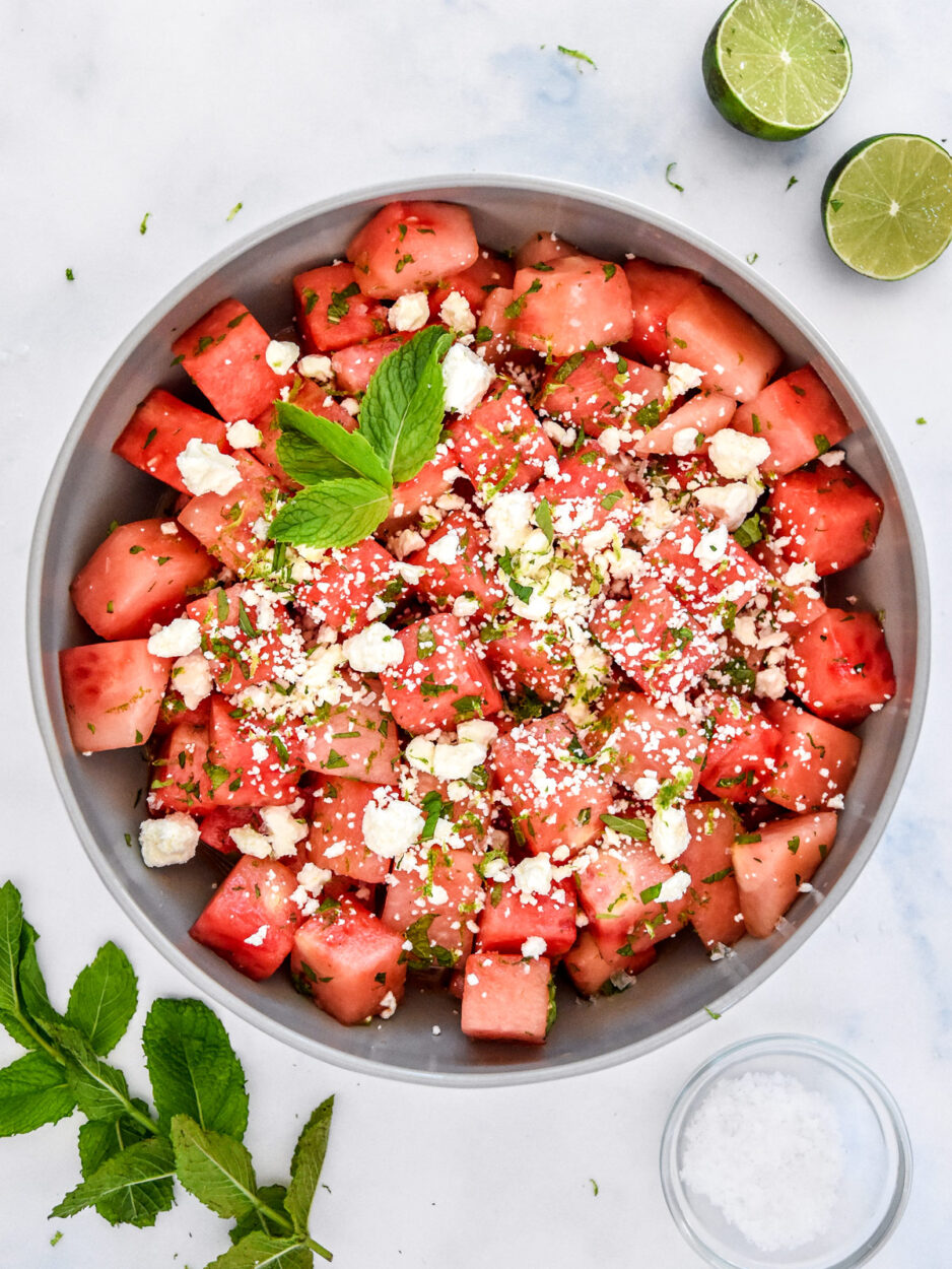 Close-up overhead shot of the finished watermelon feta mint salad in a rustic ceramic bowl, showing the beautiful color contrast and fresh herbs, with a silver spoon beside it