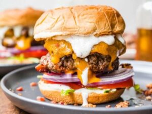 Bacon Ranch Burgers stacked high on a brioche bun with melted cheddar, crispy bacon, fresh lettuce, tomato, and a drizzle of ranch dressing on a rustic wooden board