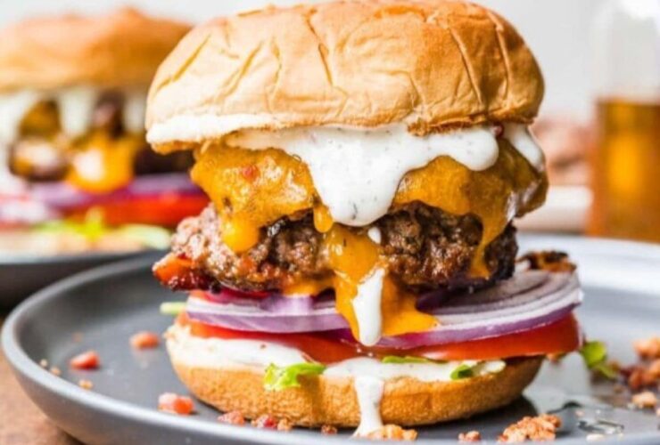 Bacon Ranch Burgers stacked high on a brioche bun with melted cheddar, crispy bacon, fresh lettuce, tomato, and a drizzle of ranch dressing on a rustic wooden board