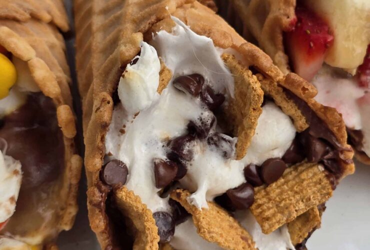 Campfire cone s'mores wrapped in foil resting over glowing campfire coals, one unwrapped to reveal melted chocolate, golden marshmallows, and fresh strawberries spilling from a crispy waffle cone
