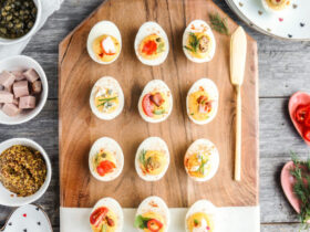 Classic deviled eggs arranged on a white marble platter, creamy yellow filling piped in neat swirls, dusted generously with smoked paprika and garnished with fresh chives, bright natural lighting, appetizing overhead shot