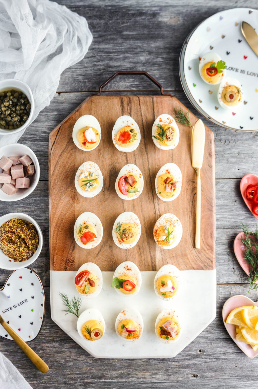Classic deviled eggs arranged on a white marble platter, creamy yellow filling piped in neat swirls, dusted generously with smoked paprika and garnished with fresh chives, bright natural lighting, appetizing overhead shot