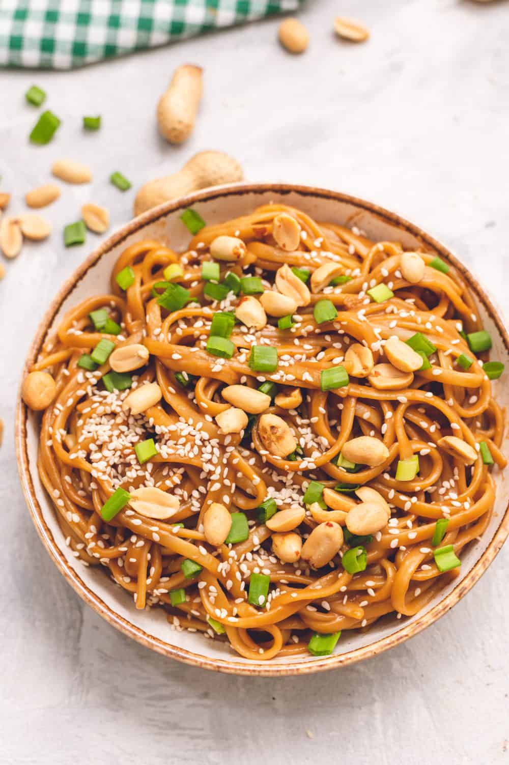 Flat lay of cold sesame noodle ingredients — peanut butter, sesame oil, soy sauce, chili oil, rice vinegar, garlic, ginger, and dry noodles arranged on a wooden cutting board