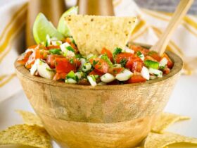 Fresh pico de gallo in a rustic clay bowl, surrounded by tortilla chips and lime wedges on a wooden board, bright natural lighting