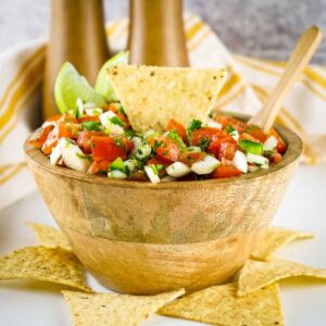 Fresh pico de gallo in a rustic clay bowl, surrounded by tortilla chips and lime wedges on a wooden board, bright natural lighting