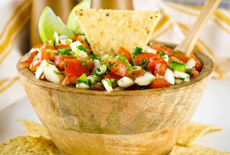 Fresh pico de gallo in a rustic clay bowl, surrounded by tortilla chips and lime wedges on a wooden board, bright natural lighting
