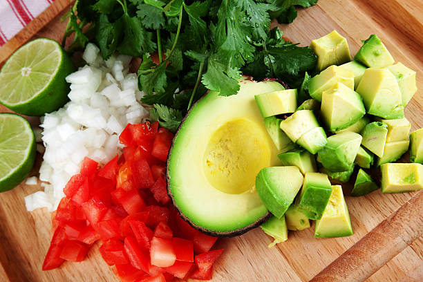Chopped tomatoes, diced white onion, sliced jalapeños, fresh cilantro, and lime halves arranged on a wooden cutting board — ingredients shot, overhead view