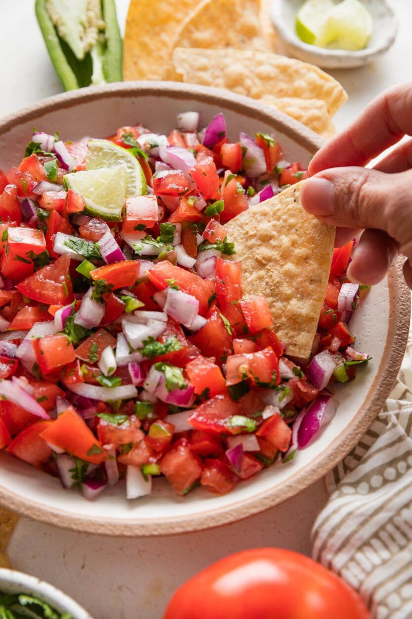 Close-up of fresh pico de gallo being scooped with a tortilla chip, showing the vibrant red tomatoes, green cilantro, and glistening lime juice, moody natural light