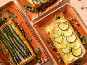 Grilled vegetable and goat cheese tart sliced on a rustic wooden board, showing charred zucchini, bell peppers, and eggplant on a creamy goat cheese filling in a golden whole wheat crust, garnished with fresh thyme and a drizzle of olive oil