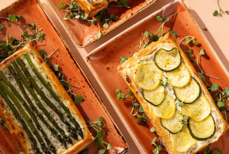 Grilled vegetable and goat cheese tart sliced on a rustic wooden board, showing charred zucchini, bell peppers, and eggplant on a creamy goat cheese filling in a golden whole wheat crust, garnished with fresh thyme and a drizzle of olive oil