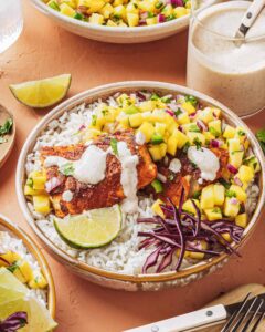 Peach mango salsa in a white bowl garnished with fresh cilantro and lime wedges, served alongside grilled fish tacos on a rustic wooden board