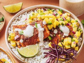 Peach mango salsa in a white bowl garnished with fresh cilantro and lime wedges, served alongside grilled fish tacos on a rustic wooden board