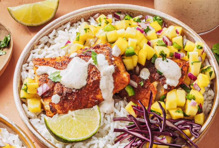Peach mango salsa in a white bowl garnished with fresh cilantro and lime wedges, served alongside grilled fish tacos on a rustic wooden board