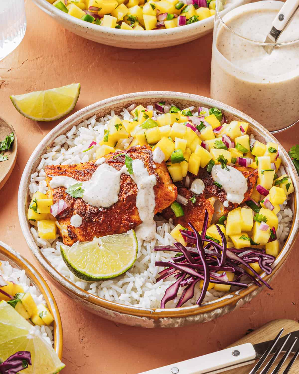Peach mango salsa in a white bowl garnished with fresh cilantro and lime wedges, served alongside grilled fish tacos on a rustic wooden board