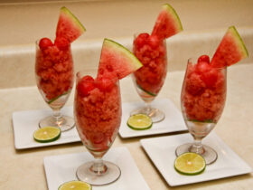 Watermelon lime granita served in chilled glasses with fresh lime wedges and mint leaves on a rustic wooden table in bright summer light