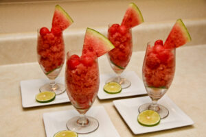 Watermelon lime granita served in chilled glasses with fresh lime wedges and mint leaves on a rustic wooden table in bright summer light
