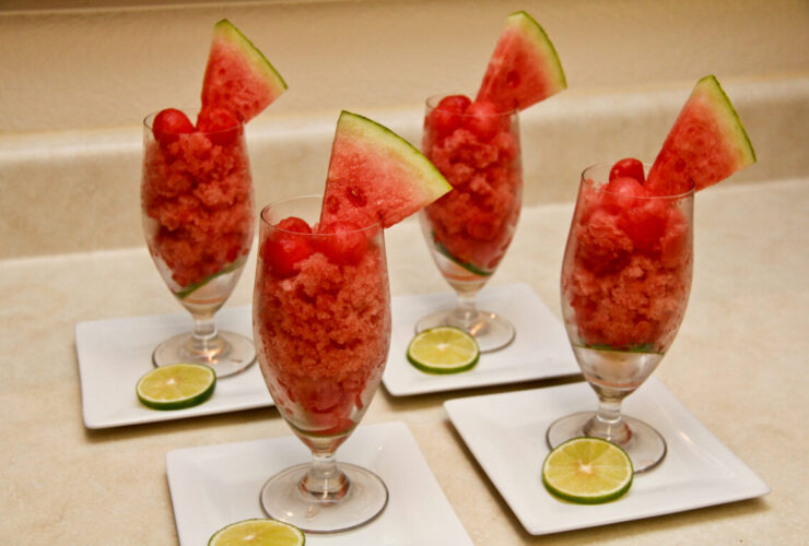 Watermelon lime granita served in chilled glasses with fresh lime wedges and mint leaves on a rustic wooden table in bright summer light