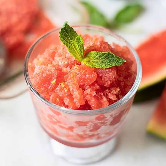 Close-up of watermelon lime granita piled high in a chilled glass with visible ice crystals, garnished with a lime wheel and fresh mint sprig