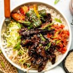 Korean beef bulgogi beautifully plated with steamed rice, lettuce wraps, and traditional banchan side dishes on a wooden table