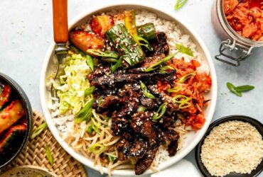 Korean beef bulgogi beautifully plated with steamed rice, lettuce wraps, and traditional banchan side dishes on a wooden table
