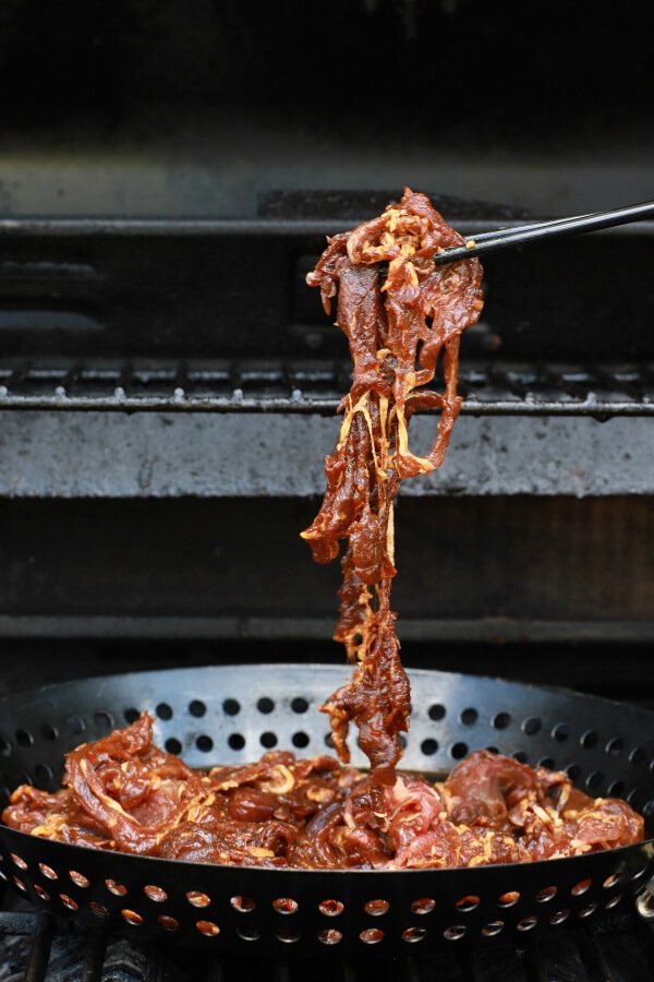 Step-by-step shot showing thinly sliced raw beef being mixed with bulgogi marinade ingredients in a glass bowl