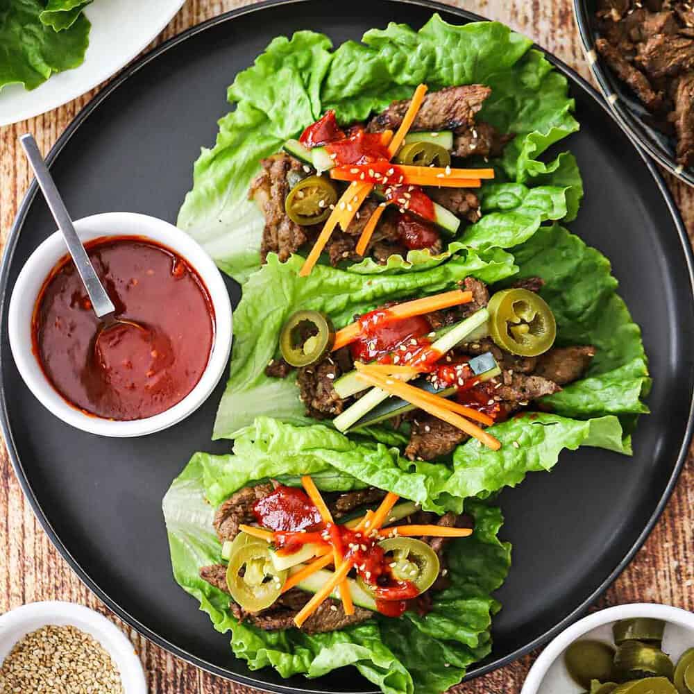 Close-up shot of beef bulgogi served in lettuce wraps with sliced green onions and sesame seeds, showing the caramelized edges of the meat