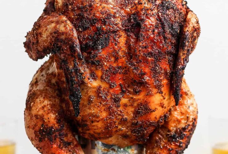 Beer Can Chicken finished dish — whole golden crispy grilled chicken standing upright on a beer can, plated on a wooden cutting board with fresh herbs and lemon slices