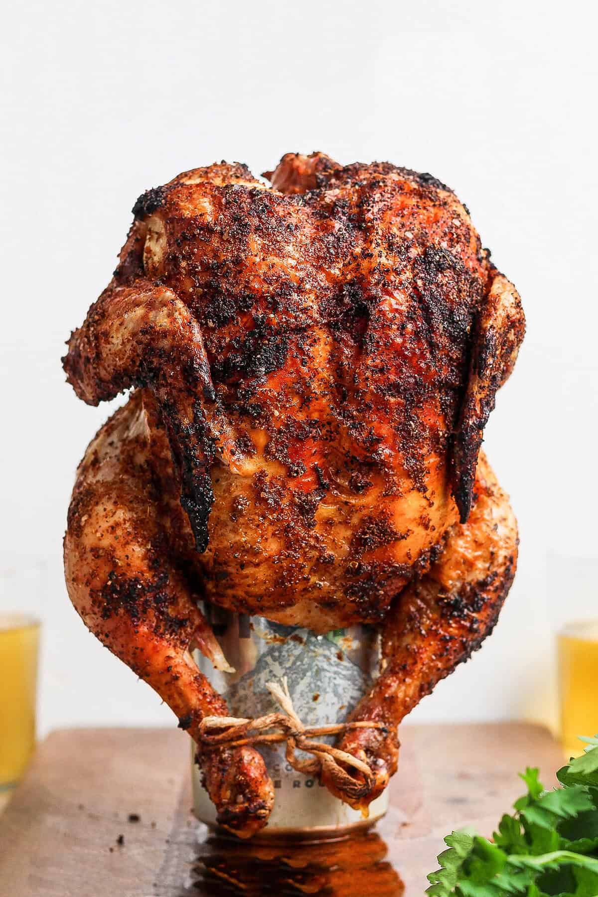 Beer Can Chicken finished dish — whole golden crispy grilled chicken standing upright on a beer can, plated on a wooden cutting board with fresh herbs and lemon slices