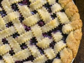 Golden lattice-top blueberry pie cooling on a wire rack, deep purple filling bubbling through the woven crust, dusted with coarse sugar, summer sunlight overhead