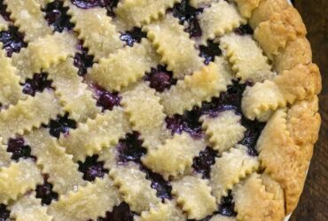 Golden lattice-top blueberry pie cooling on a wire rack, deep purple filling bubbling through the woven crust, dusted with coarse sugar, summer sunlight overhead